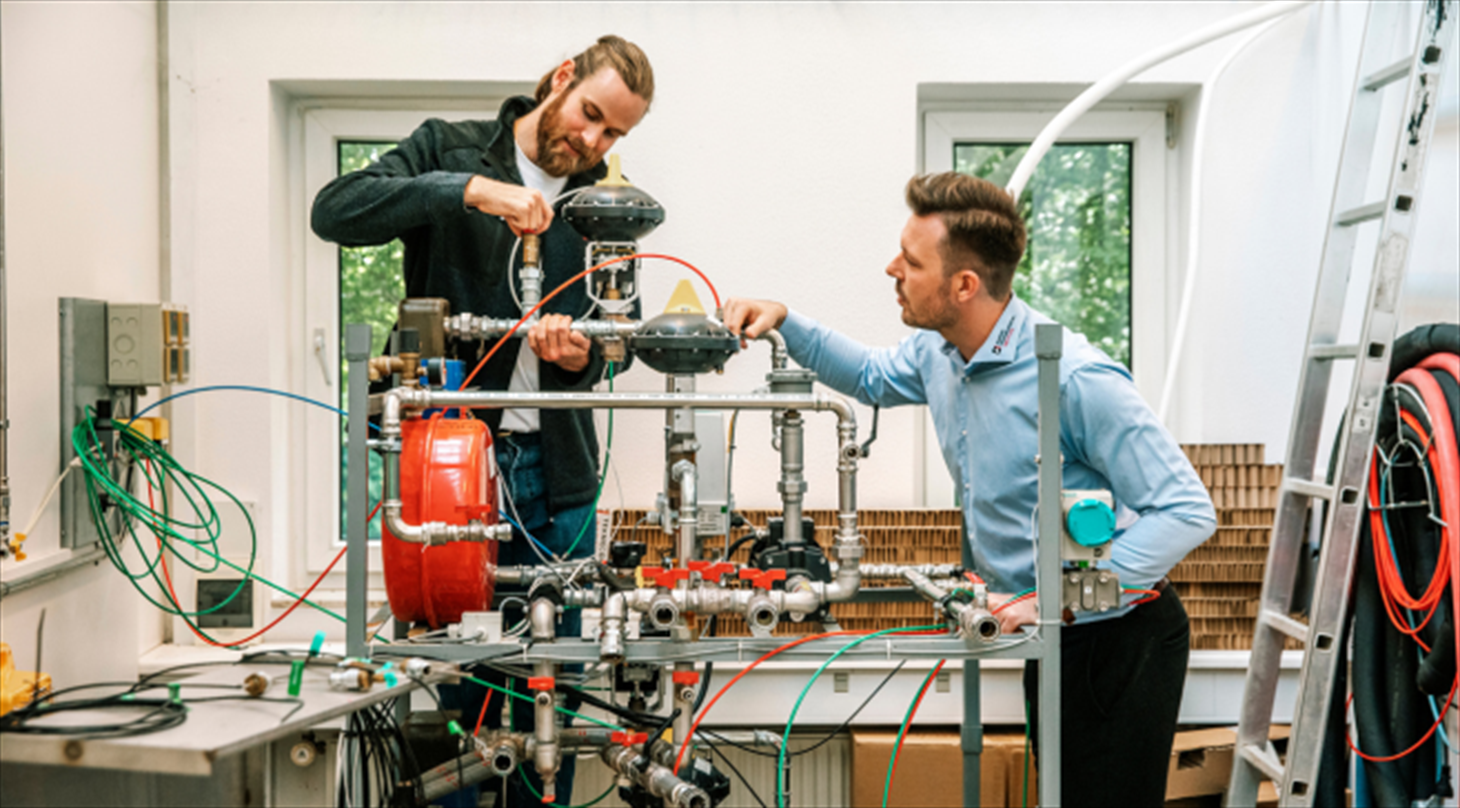 The picture shows a test ring for testing of domestic hot water heat pumps and two test engineers in the Heat Pump Test Laboratory at Danish Technological Institute